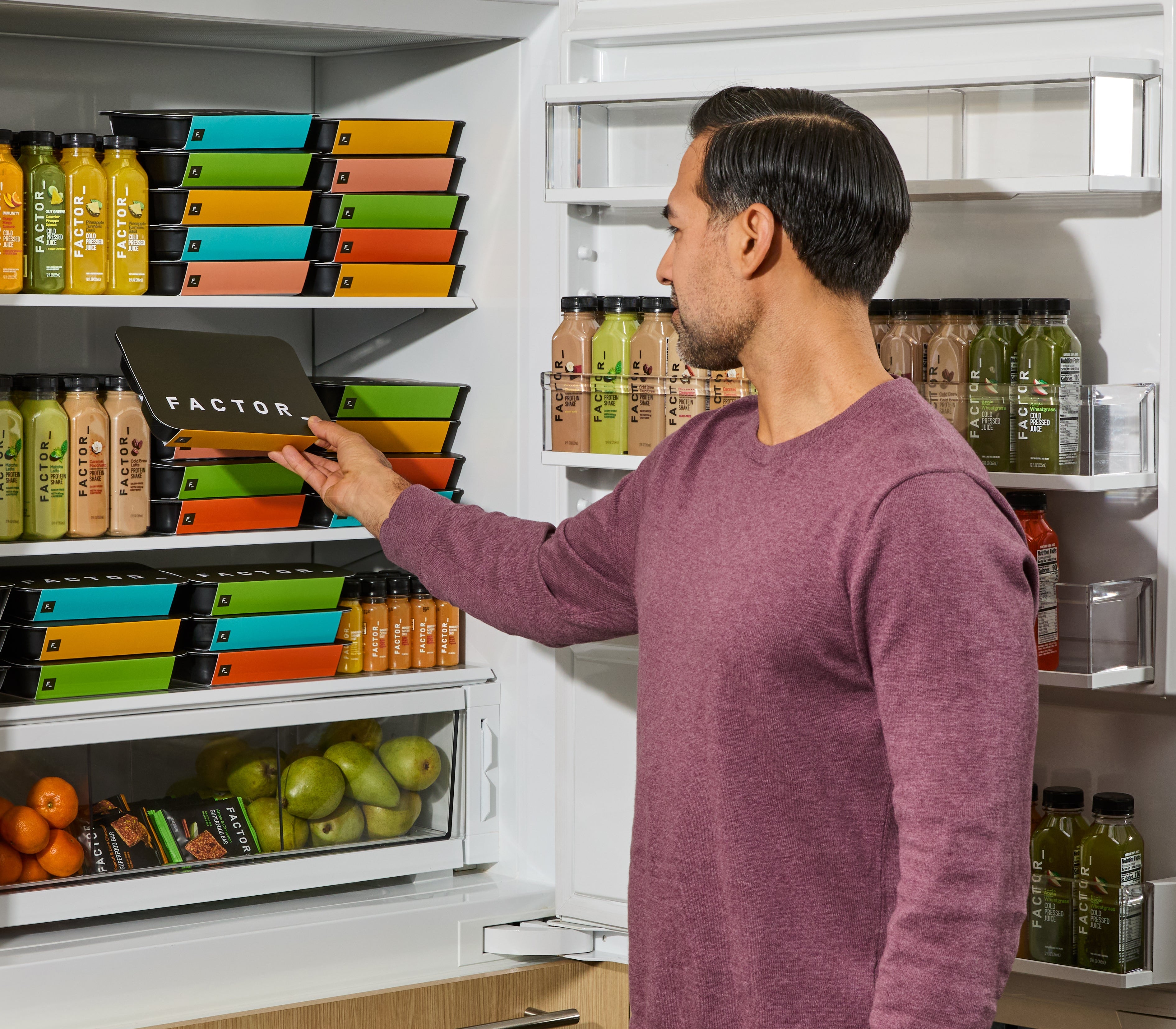 Man interacting with a smart refrigerator filled with food and drinks.